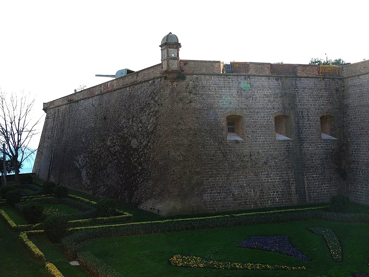 The thick stone walls of Montjuïc Castle rising above its moat and gardens