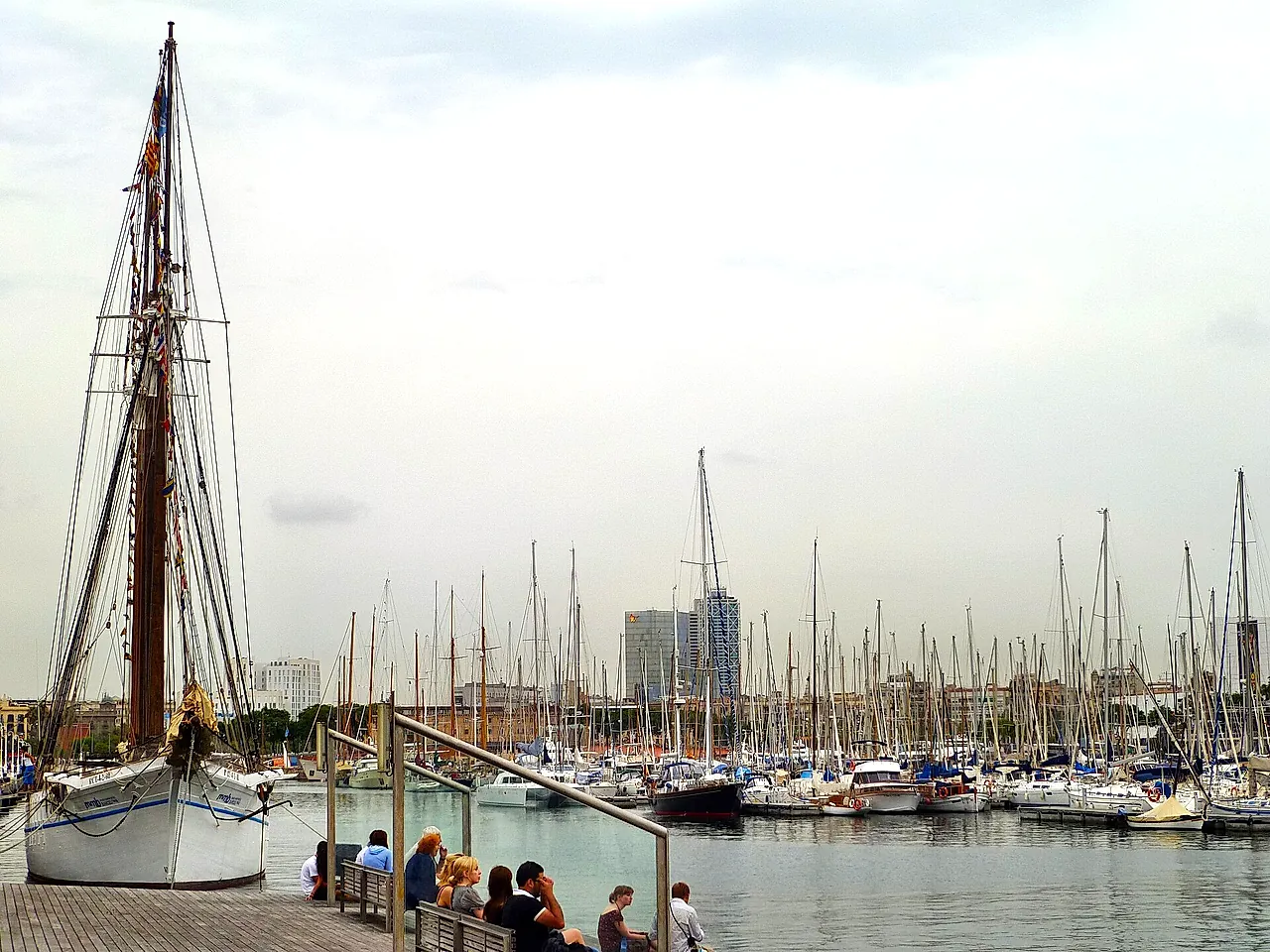 Sailing boats moored in the marina of Port Vell, with a tall wooden mast in the foreground
